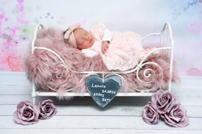 Die kleine Leonie hat ein rosa Spitzenkleid an und liegt in einem weißen Bettchen.